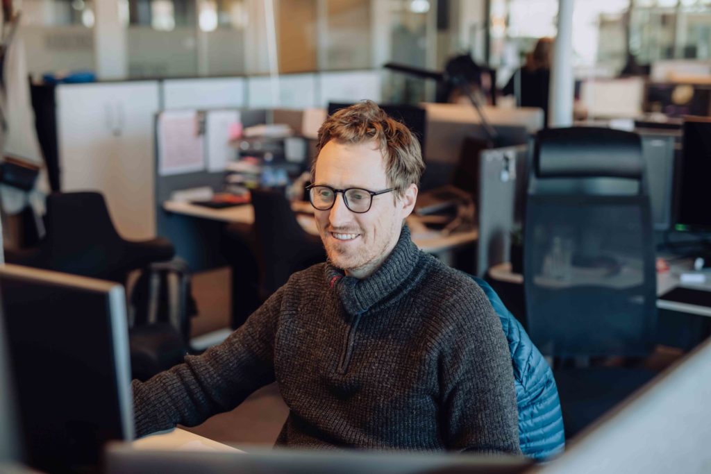En mann med briller sitter foran en pc-skjerm og jobber.